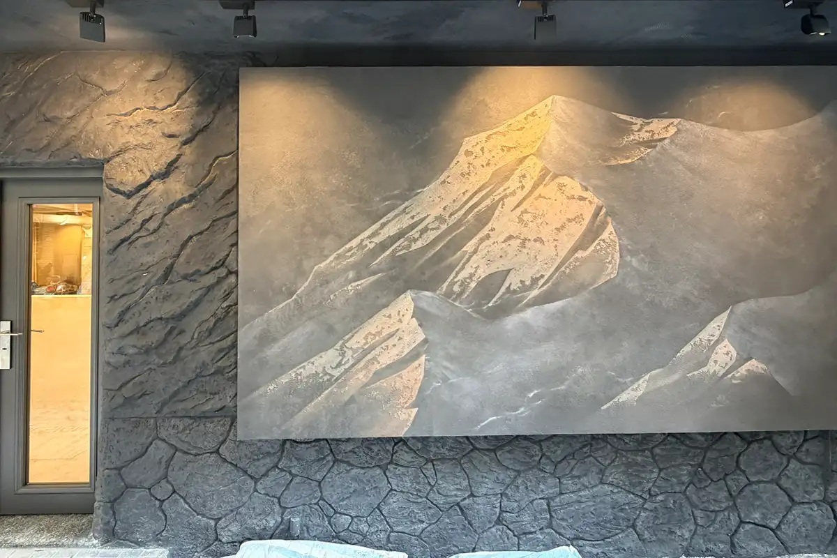 深灰色外牆,中央為山峰造型的大幅立體牆面,左側為岩石紋理與玻璃門,下方為石塊紋路