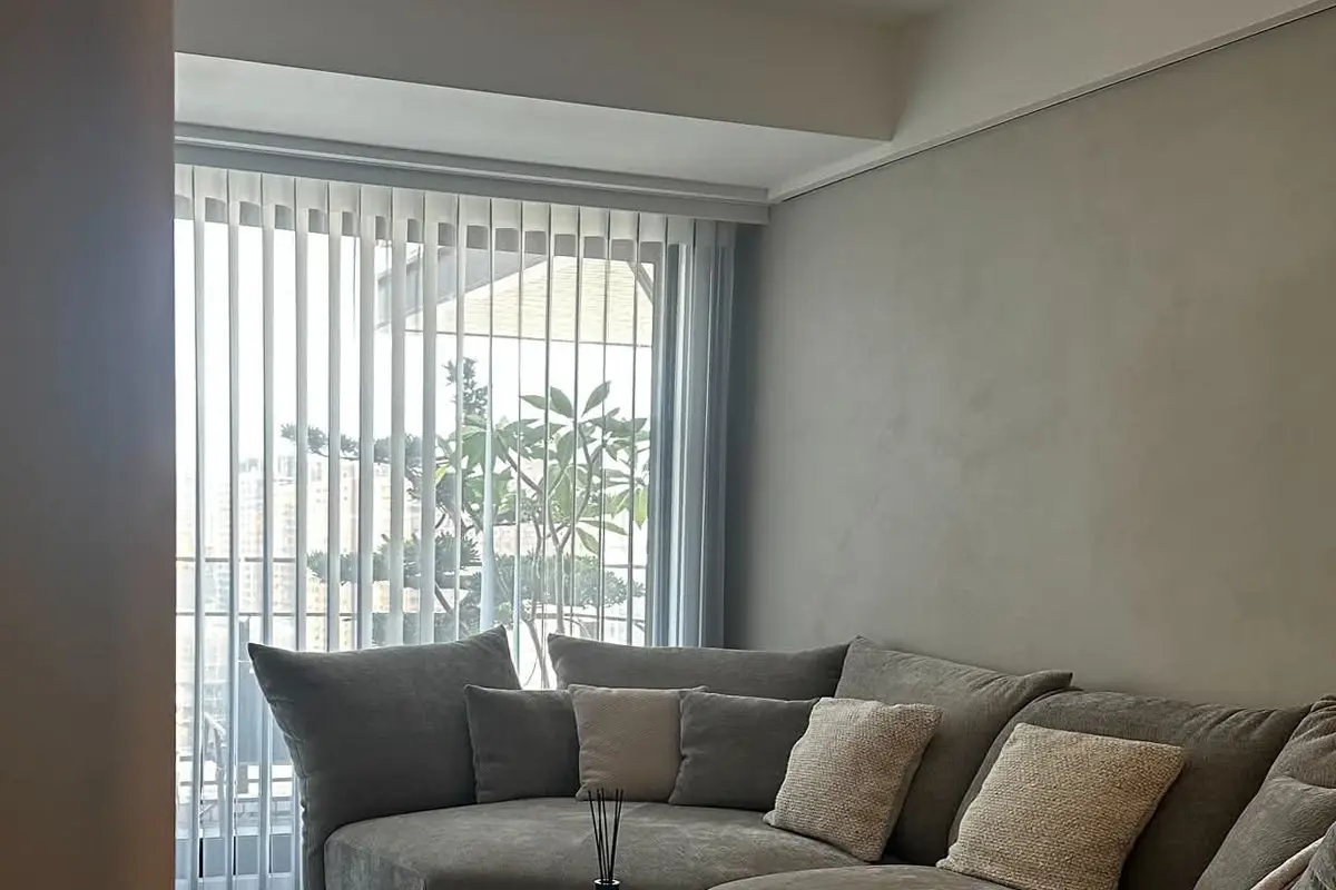 客廳淺灰色無縫牆面帶細緻雲紋,前方為灰色布沙發,左側為落地窗與直立百葉簾