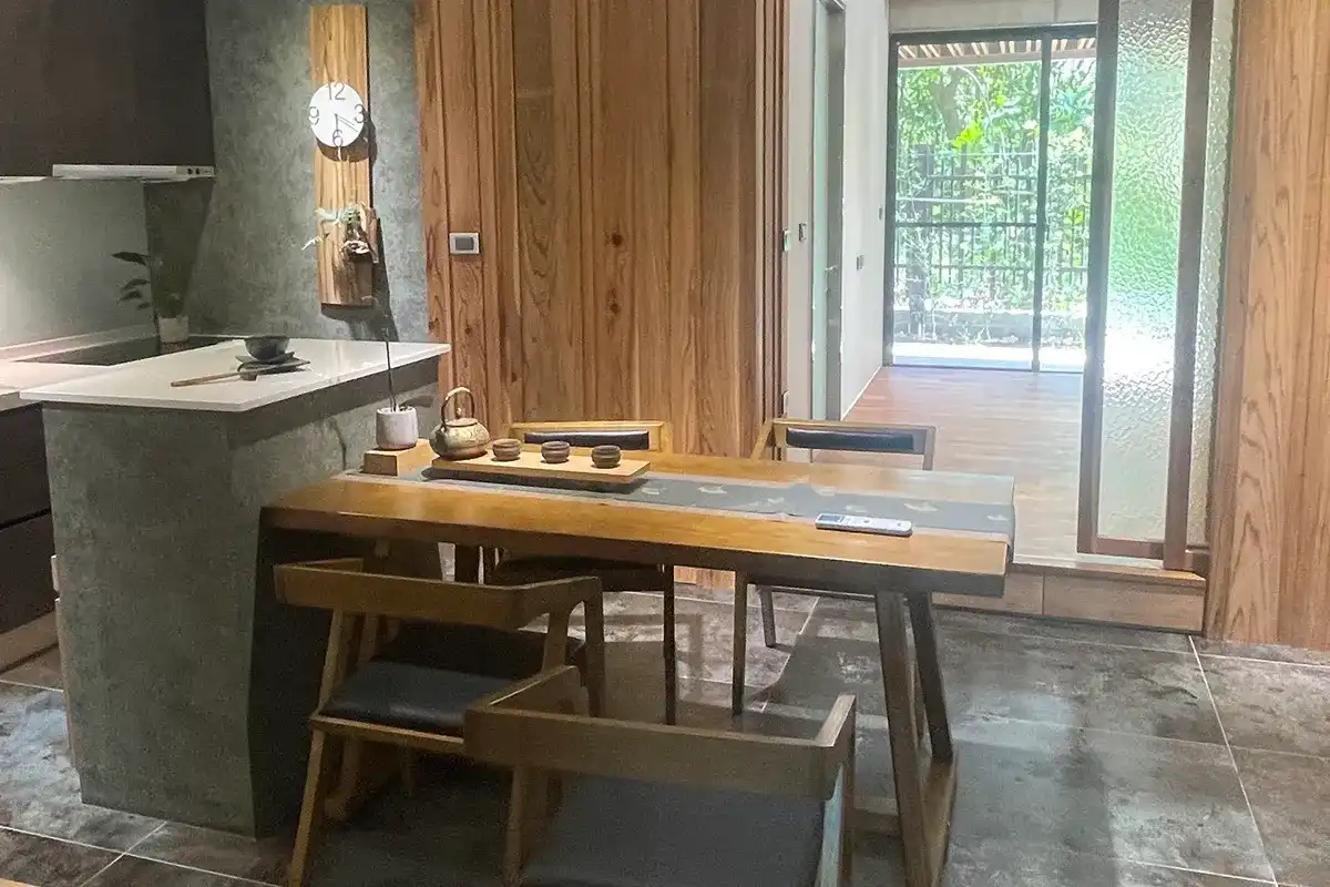 住家廚房,牆面與中島基座為灰綠色礦物質感,前方為原木餐桌