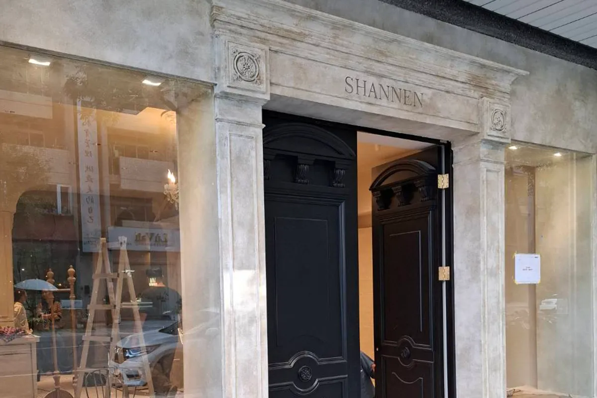 法式復古風店面,門框與櫥窗外牆為灰白色礦物質感,中央為黑色木門