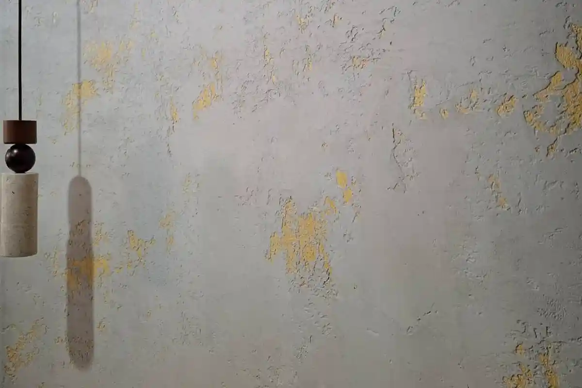 灰色斑駁牆面上點綴金色箔片，左側垂掛一盞吊燈